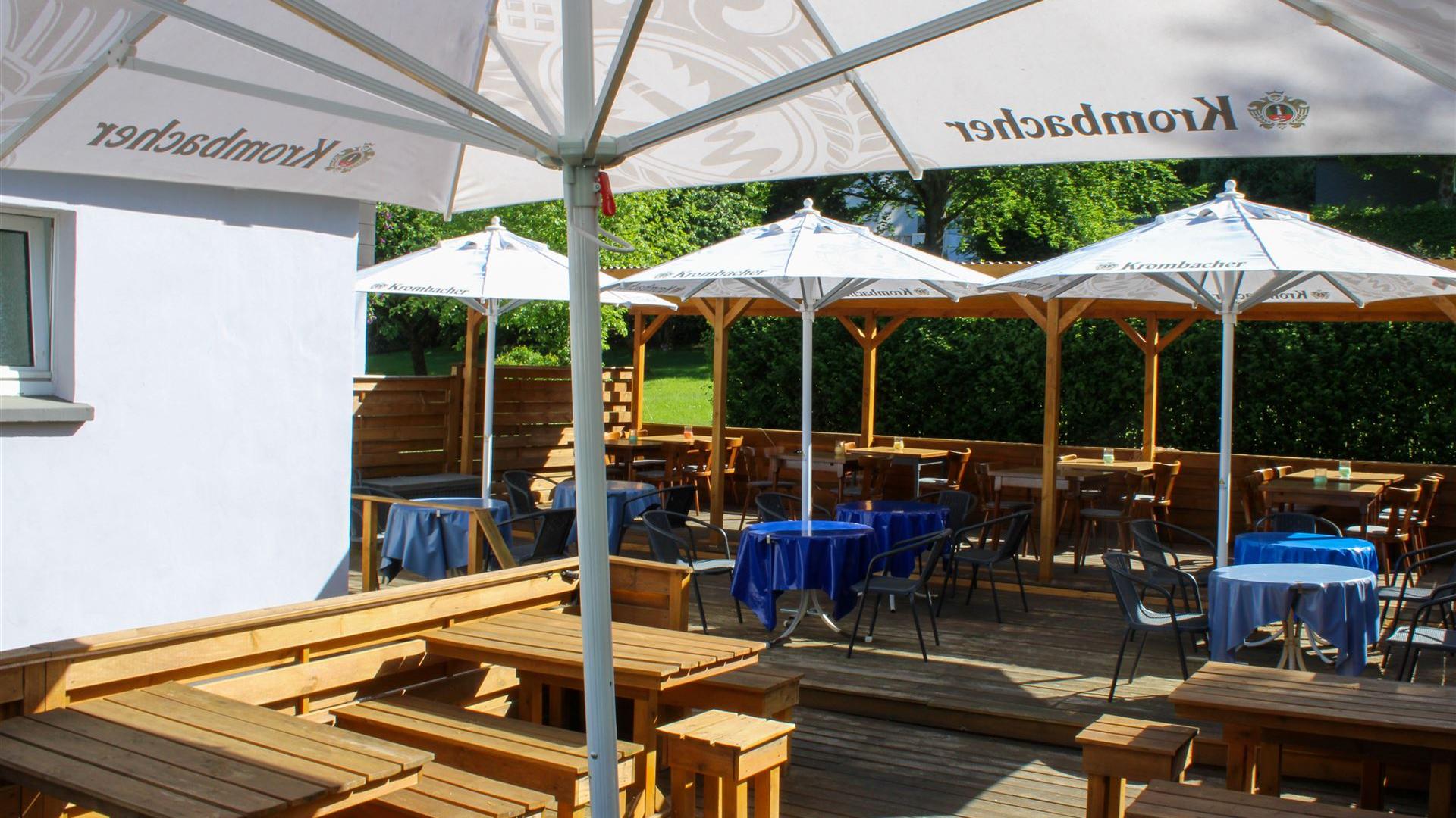 Das Bild zeigt die Terrasse mit Krombacher Schirmen und bei schönem Wetter