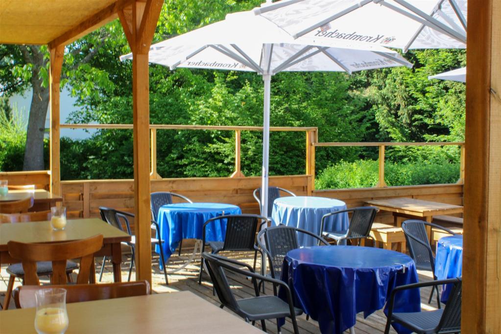Das Bild zeigt die Terrasse bei schönem Wetter und ausgeklaptten Krombacher Sonnenschirme