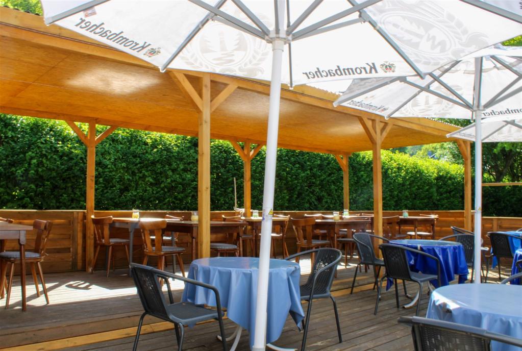 Das Bild zeigt die Terrasse bei schönem Wetter und ausgeklaptten Krombacher Sonnenschirme aus einer anderen Ecke fotografiert